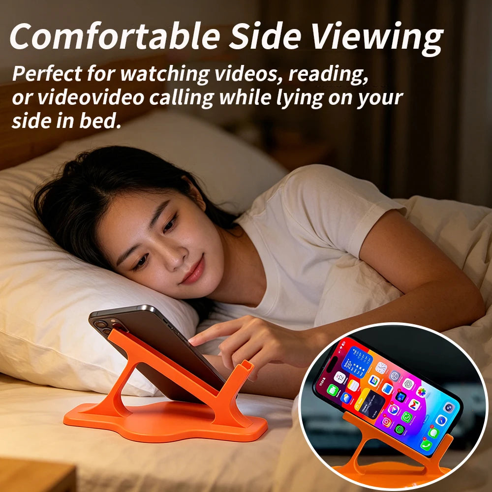 Person lying on their side in bed watching a phone on a small orange folding stand