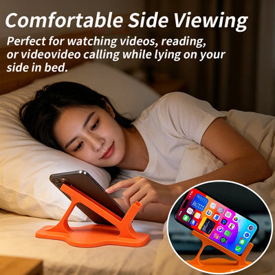 Person lying on their side in bed watching a phone on a small orange folding stand